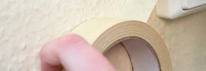 Hand klebt Malerkrepp an eine Wand